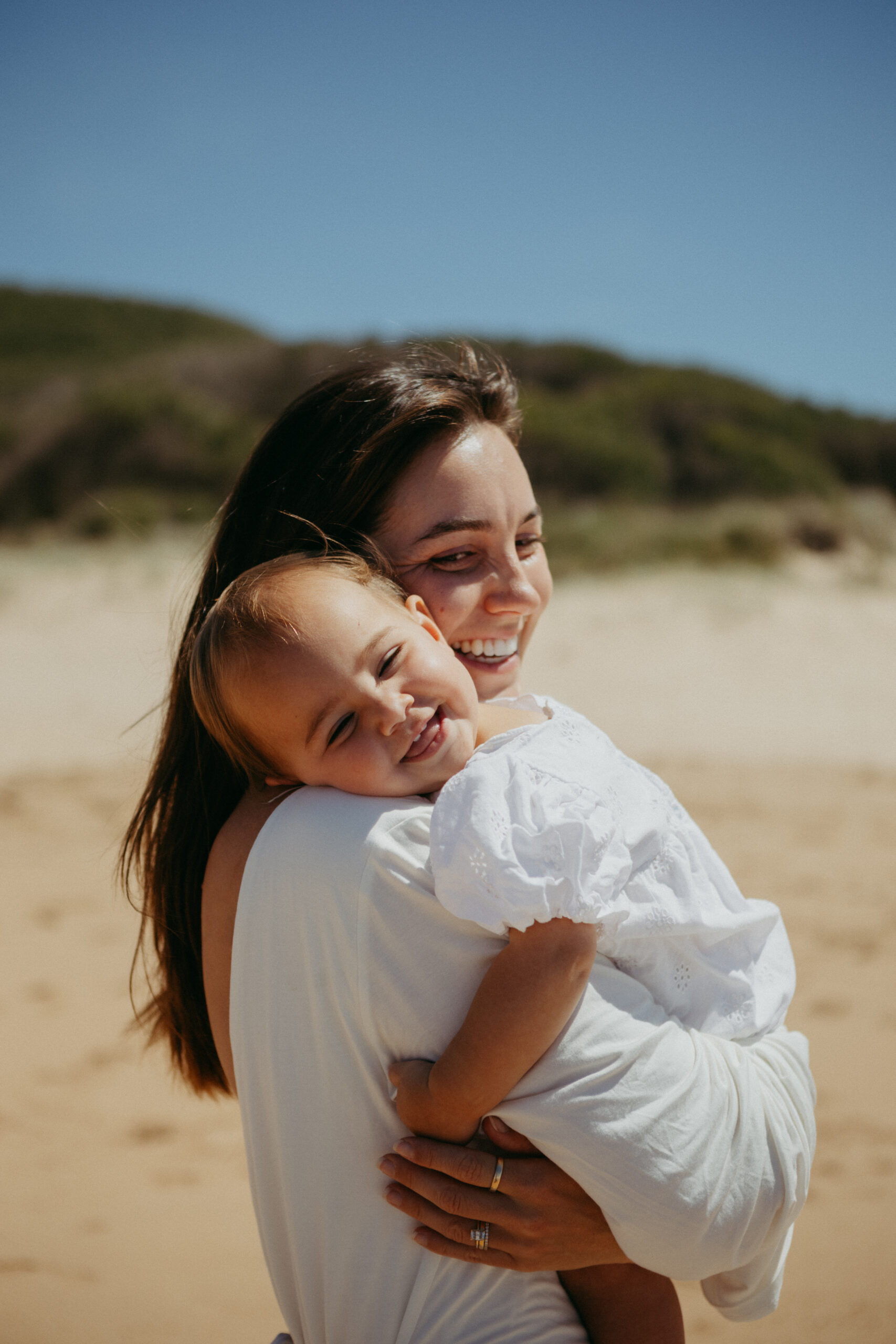 mum holding daughter smiling walking along wollongong beach photoshoot
